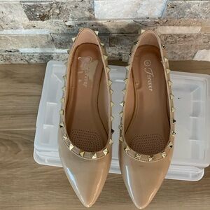 Man made patten leather look light beige flats with studs .